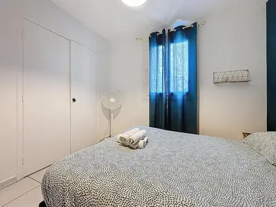a bedroom with a bed with blue curtains and a fan at Le Brooklyn - Appartement rez de chaussée - Wifi in Narbonne