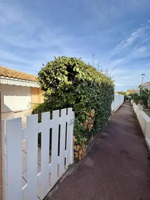 a white fence with a large green hedge at Pavillon avec piscine à deux pas de la plage in Gruissan