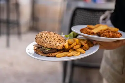 a person holding two plates with a hamburger and french fries at Camping La Tour de France in Latour-de-France