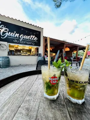 two drinks sitting on a wooden table in front of a store at Camping La Tour de France in Latour-de-France