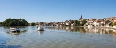 two boats on a river with a town in the background at YZA Lodge 2026 in Castelnaudary