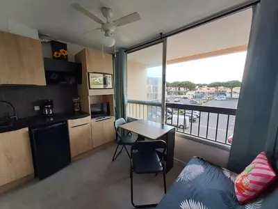 a living room with a table and a kitchen with a balcony at Studio rénové avec piscine et accès direct plage in Gruissan