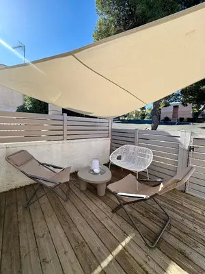 two chairs and a table under an umbrella on a deck at Pavillon rénové avec terrasse & piscine in Gruissan