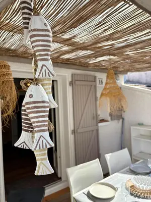 a dining room with a table with white chairs and a ceiling with striped towels at Pavillon rénové avec terrasse & piscine in Gruissan