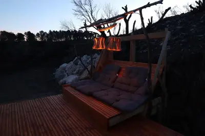 a porch swing with a couch and lights on it at L'Amoré - Cabane en A avec spa privatif in Durban-Corbières