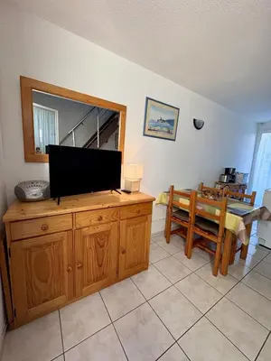 a living room with a television on a dresser and a table at Pavillon familial à deux pas de la plage in Gruissan