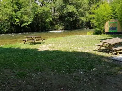 two picnic tables in a field next to a river at Bungalow toilé avec terrasse jusqu'à 5 personnes - API-1-52-1480 in Axat