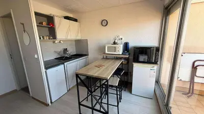 a small kitchen with a table and a microwave at AIG168 GRUISSAN STUDIO VUE PORT AVEC TERRASSE PARKING ET PISCINES in Gruissan