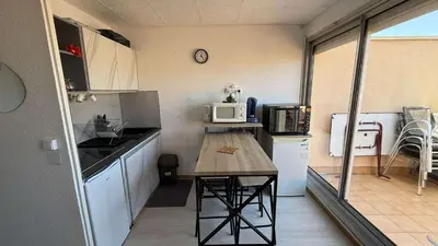 a small kitchen with a table and a microwave at AIG168 GRUISSAN STUDIO VUE PORT AVEC TERRASSE PARKING ET PISCINES in Gruissan