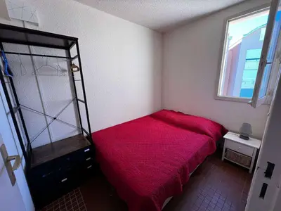 a small bedroom with a red bed and a window at AIG_42 Appartement Type 2 – 4 couchages – Superbe vue avant-port à Gruissan in Gruissan