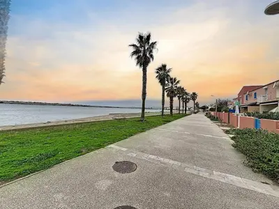 a sidewalk with palm trees on the side of a beach at Villa Closia - Maison de vacances à 50mètres de la plage - Climatisation et Wifi in Gruissan