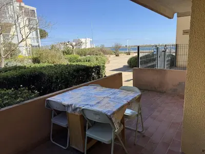 a table and chairs on a patio with a view of the ocean at AIG 52 – Appartement en rez-de-chaussée – Résidence de la Plage – Gruissan – 4 personnes in Gruissan