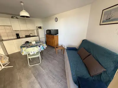 a living room with a blue couch and a kitchen at AIG 52 – Appartement en rez-de-chaussée – Résidence de la Plage – Gruissan – 4 personnes in Gruissan