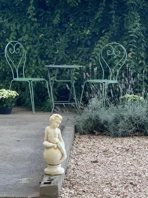 a statue of a child sitting in a garden with two chairs at La Maison Jolie bnb in Puicheric