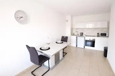 a white kitchen with a table and a clock on the wall at T2 lumineux avec parking privé in Narbonne