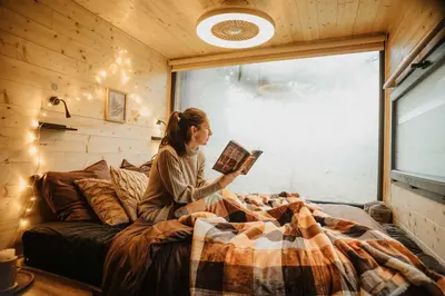 a woman sitting on a bed reading a book at Homnest - Brumes des Hauts Bains - Coeur Pyrennees in Escouloubre