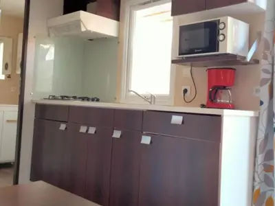 a kitchen with brown cabinets and a microwave and a window at Mobil-Home 2 Chambres avec Terrasse - API-1-52-1325 in Vielmur-sur-Agout
