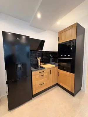 a kitchen with a black refrigerator and wooden cabinets at Charmant T2 au cœur de ville in Narbonne