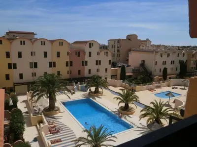 a view of a pool with palm trees and buildings at Appartement charmant avec balcon, piscine - 5 pers. - FR-1-619-159 in Gruissan