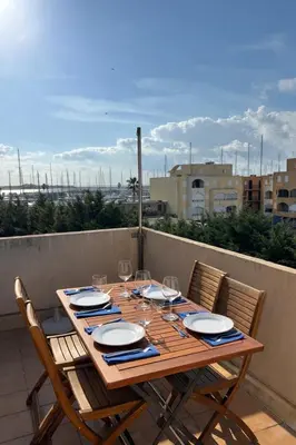 a wooden table with plates and wine glasses on a balcony at Charmant appartement proche du port in Gruissan