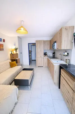 a living room with a couch and a kitchen at NOUVEAU La Grande Voile Piscine-Parking-Draps By LCG in Gruissan