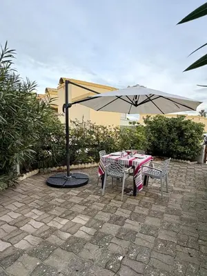 a table and chairs under an umbrella on a patio at Rez-de-jardin moderne - Accès direct plage in Gruissan