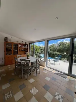 a dining room with a table and chairs and windows at Villa de charme avec piscine privée au sel in Gruissan
