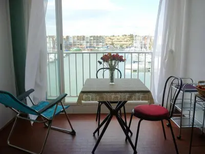 a table with chairs and a vase of flowers on a balcony at Studio cabine – 2 couchages – Vue port – Résidence Le Chébeck – Gruissan in Gruissan