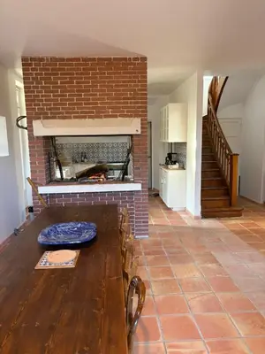 a living room with a table and a brick fireplace at Maison familiale face au lac de Saint-Ferréol in Revel