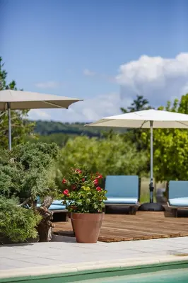 a patio with two chairs and umbrellas and a pool at Le Petit Viala in Capestang