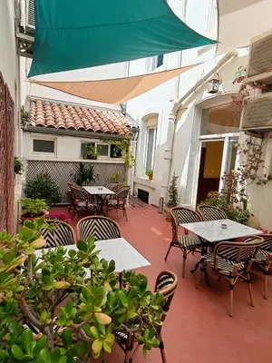 an outdoor patio with tables and chairs and a green umbrella at Hotel de France in Narbonne