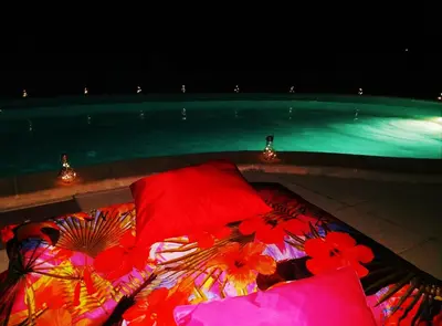 a bed with red and colorful pillows next to a swimming pool at Les chalets du Relais d'Aguilar in Tuchan