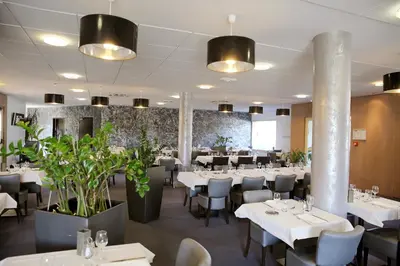a restaurant with white tables and chairs and plants at The Originals City, Hôtel Le Causséa, Castres in Castres
