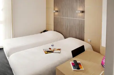 a room with two beds and a table with a remote control at The Originals City, Hôtel Le Causséa, Castres in Castres