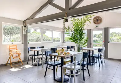 a dining room with tables and chairs and windows at B&B HOTEL Narbonne 1 in Narbonne