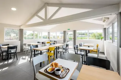 a dining room with tables and chairs and windows at B&B HOTEL Narbonne 1 in Narbonne