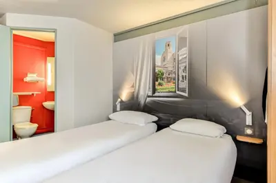 two twin beds in a room with a bathroom at B&B HOTEL Narbonne 2 in Narbonne