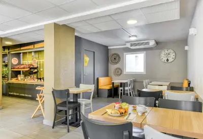 a restaurant with tables and chairs and a clock on the wall at B&B HOTEL Narbonne 2 in Narbonne