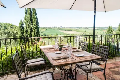 a wooden table with chairs and an umbrella on a balcony at Cuq en Terrasses in Cuq-Toulza