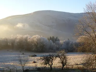 a snowy field with trees and a hill in the background at La Bouriotte Gîtes in Labastide-Rouairoux