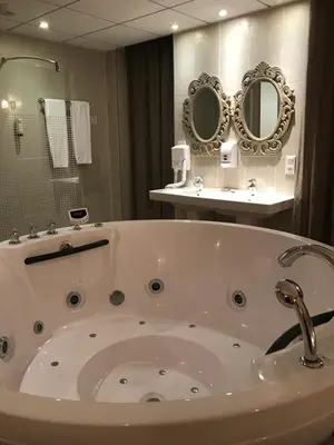a large white tub in a bathroom with two mirrors at Logis Hôtel restaurant Les Minotiers in Mirepoix