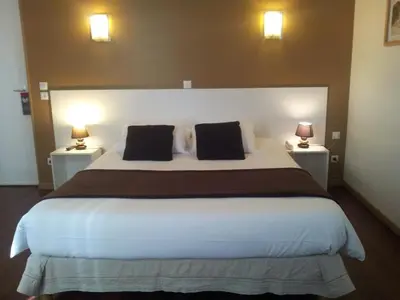 a bedroom with a large white bed with two lamps at Hôtel Du Midi in Narbonne