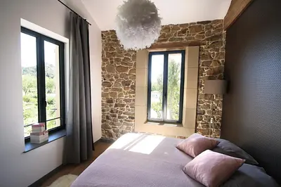 a bedroom with a bed with a stone wall and windows at La Forge in Montséret