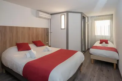 a bedroom with two beds with red and white sheets at Brit Hotel Plaisance A9/A61 in Narbonne