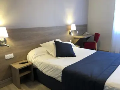 a hotel room with a large bed with a blue pillow at Hôtel Le Roi Gourmand in Pamiers
