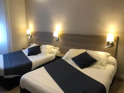 two beds in a hotel room with two lamps on the wall at Hôtel Le Roi Gourmand in Pamiers