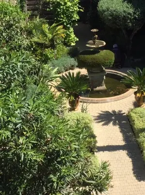 a garden with a fountain and trees and bushes at O'palmier Caché in Saint-Marcel