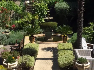 a garden with a fountain and trees and bushes at O'palmier Caché in Saint-Marcel