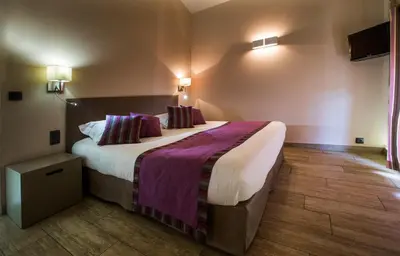 a bedroom with a large bed with purple sheets and pillows at Logis auberge restaurant Du Vigneron in Cucugnan