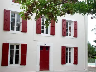 a white house with red shuttered windows and a red door at La Vadrouille in Sigean